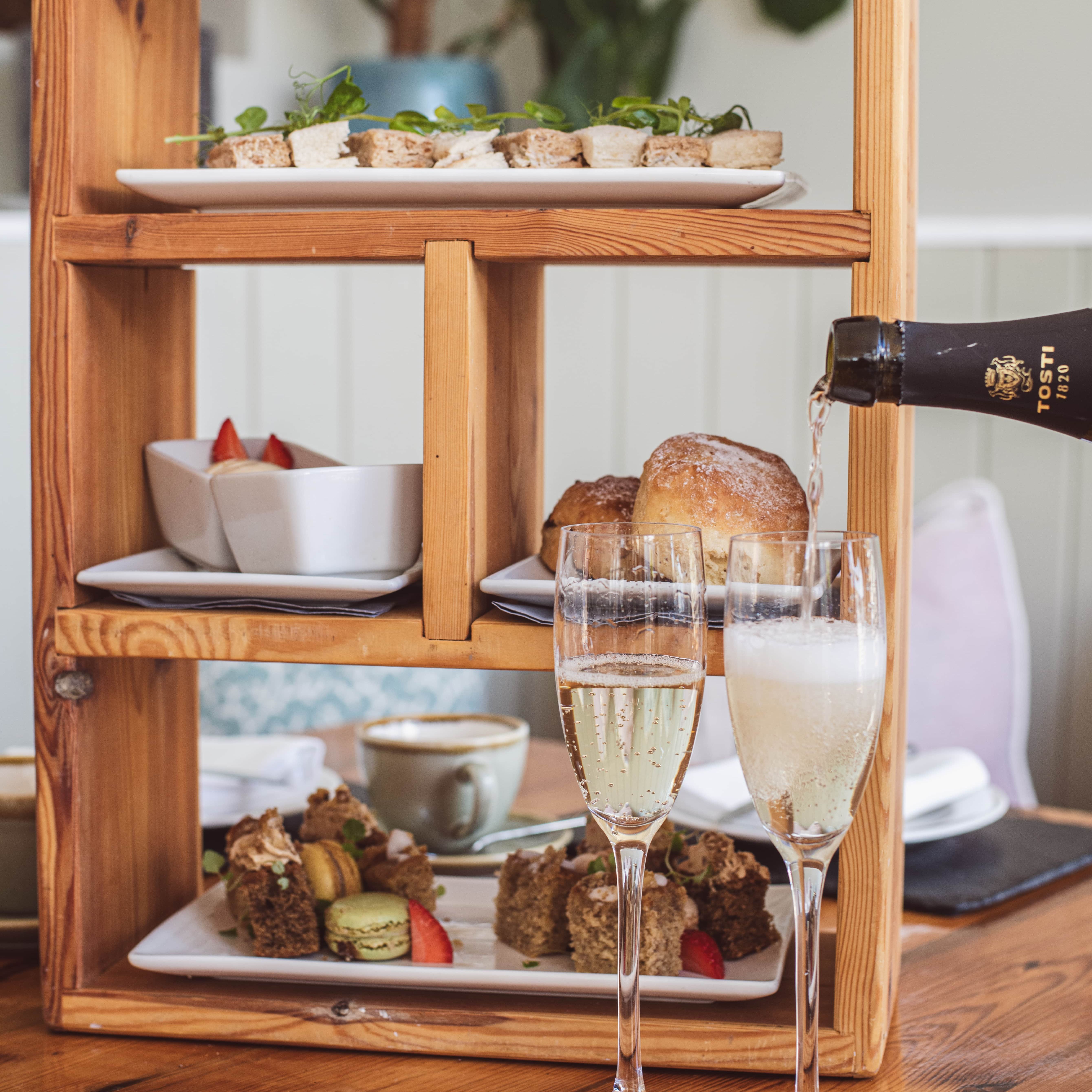 Afternoon tea set with sandwiches, desserts, scones, and sparkling wine being poured into glasses
