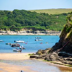 Boats floating on a blue bay with people on the beach and green hills in the background