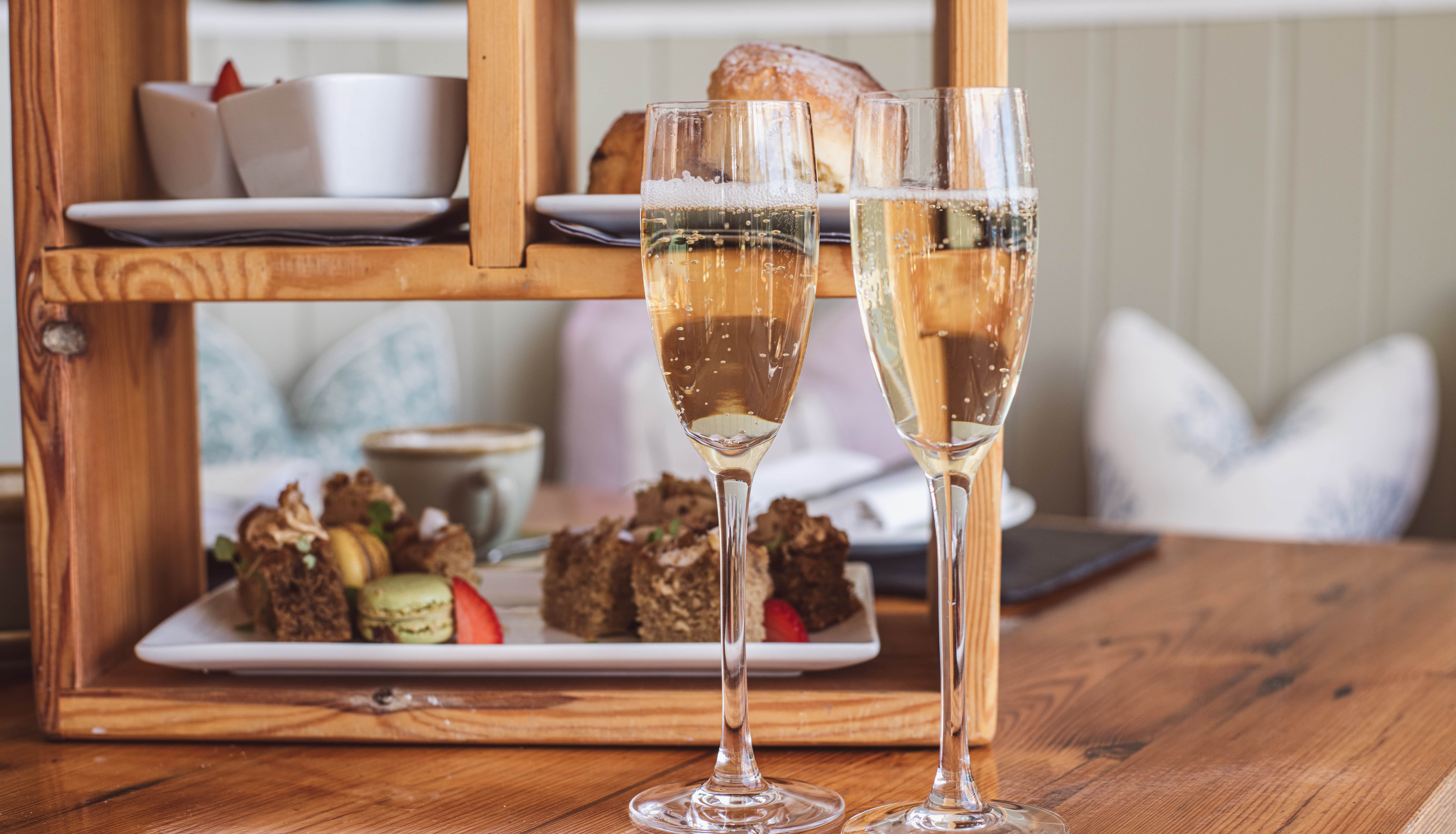Two glasses of champagne with afternoon tea desserts on a wooden table