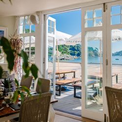 Sunny seaside restaurant with open doors leading to deck seating and ocean view