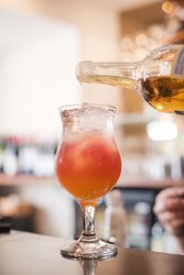 Bartender pouring liquor into a cocktail glass with ice and a colorful layered drink
