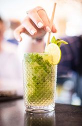 Hand stirring a mojito cocktail with mint and lime garnish in a textured glass