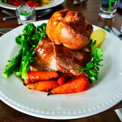 Traditional British roast dinner with roast beef, Yorkshire pudding, carrots, broccoli, and parsley on a white plate.