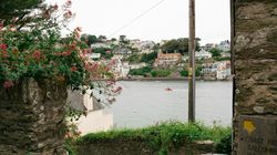 Stone steps leading down to a riverbank with a view of colorful houses across the water, surrounded by greenery and flowers.