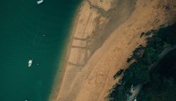 Aerial view of a sandy beach with boats on water and vehicles parked near the shoreline