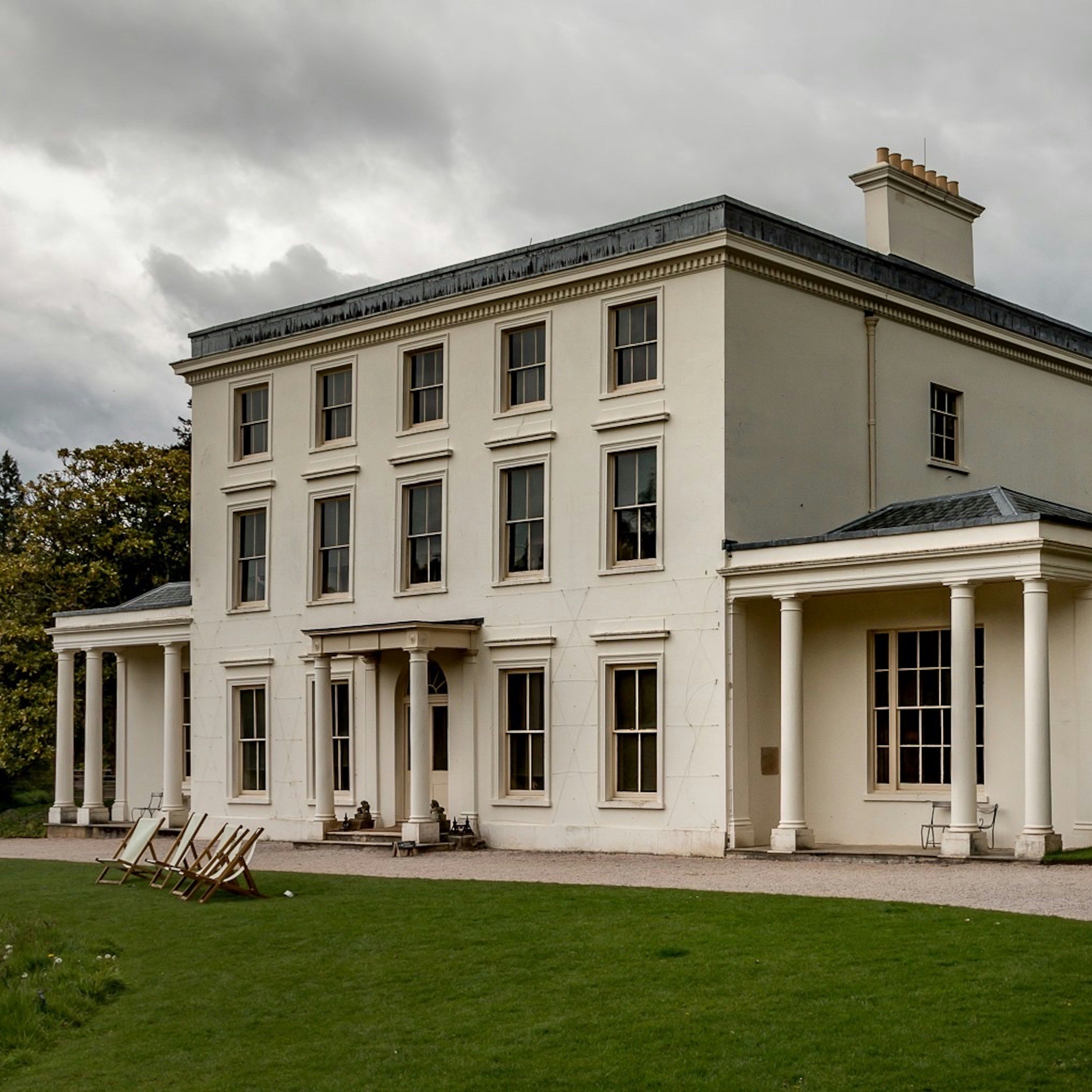 Large white historic mansion with columns, surrounded by lawn and trees.