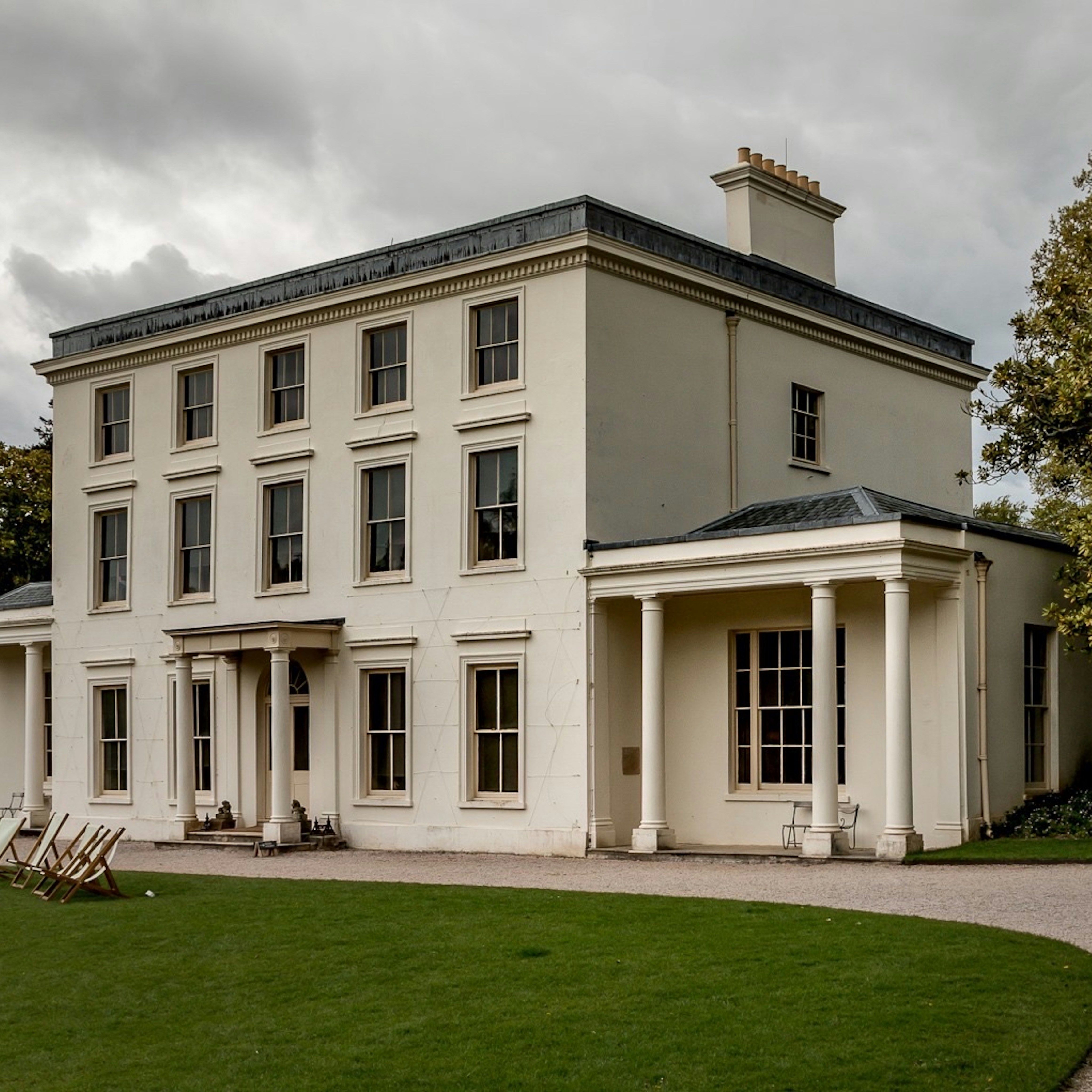Large white historic mansion with columns, surrounded by lawn and trees.