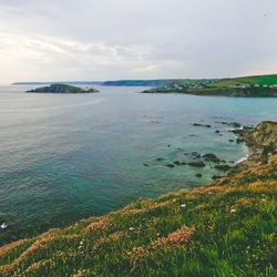 Coastal landscape with grassy cliffs overlooking a calm sea and distant headlands.