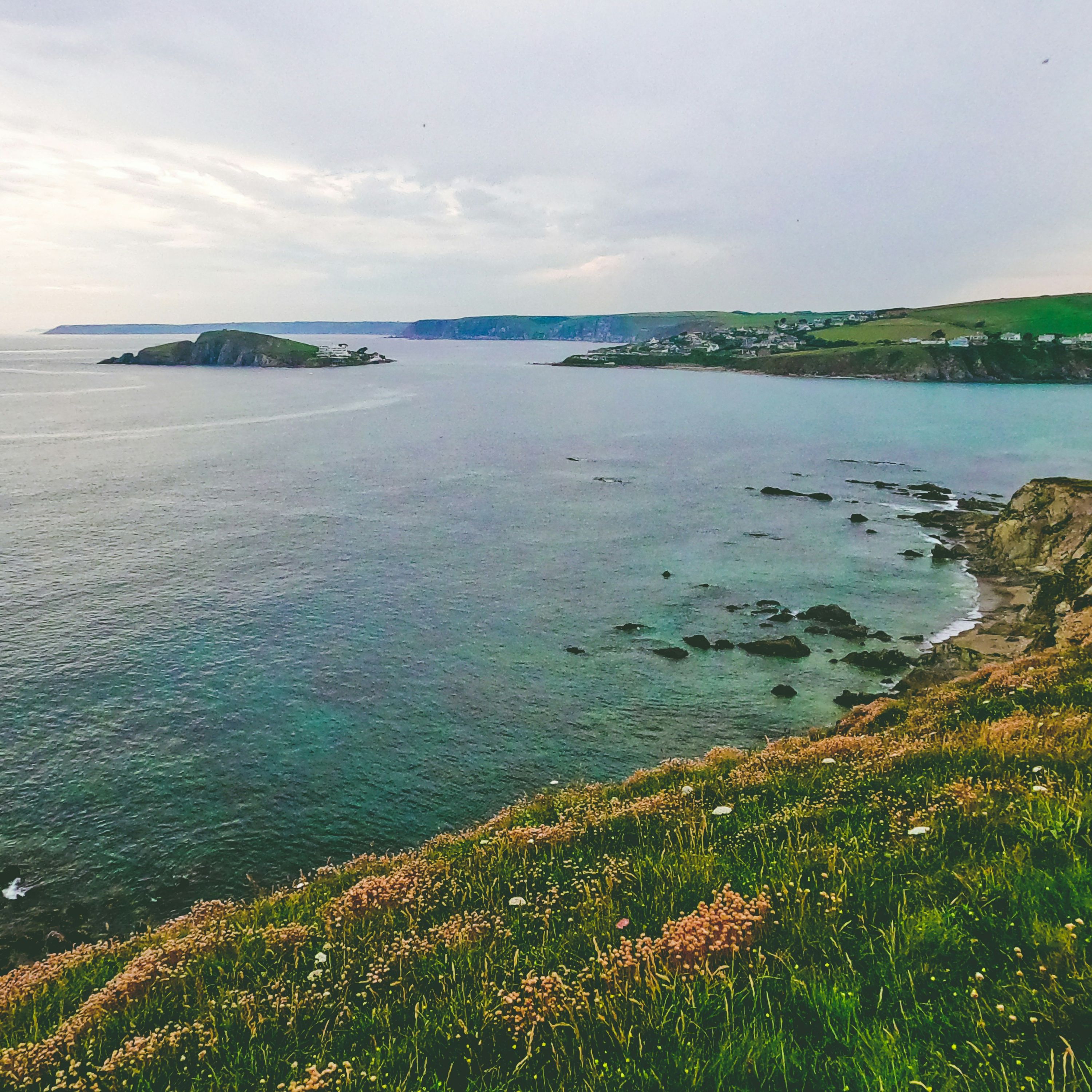 Coastal landscape with grassy cliffs overlooking a calm sea and distant headlands.