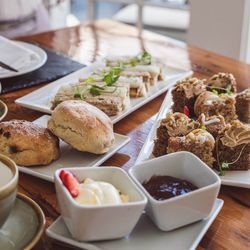 Afternoon tea with scones, finger sandwiches, cakes, clotted cream, and jam on a wooden table