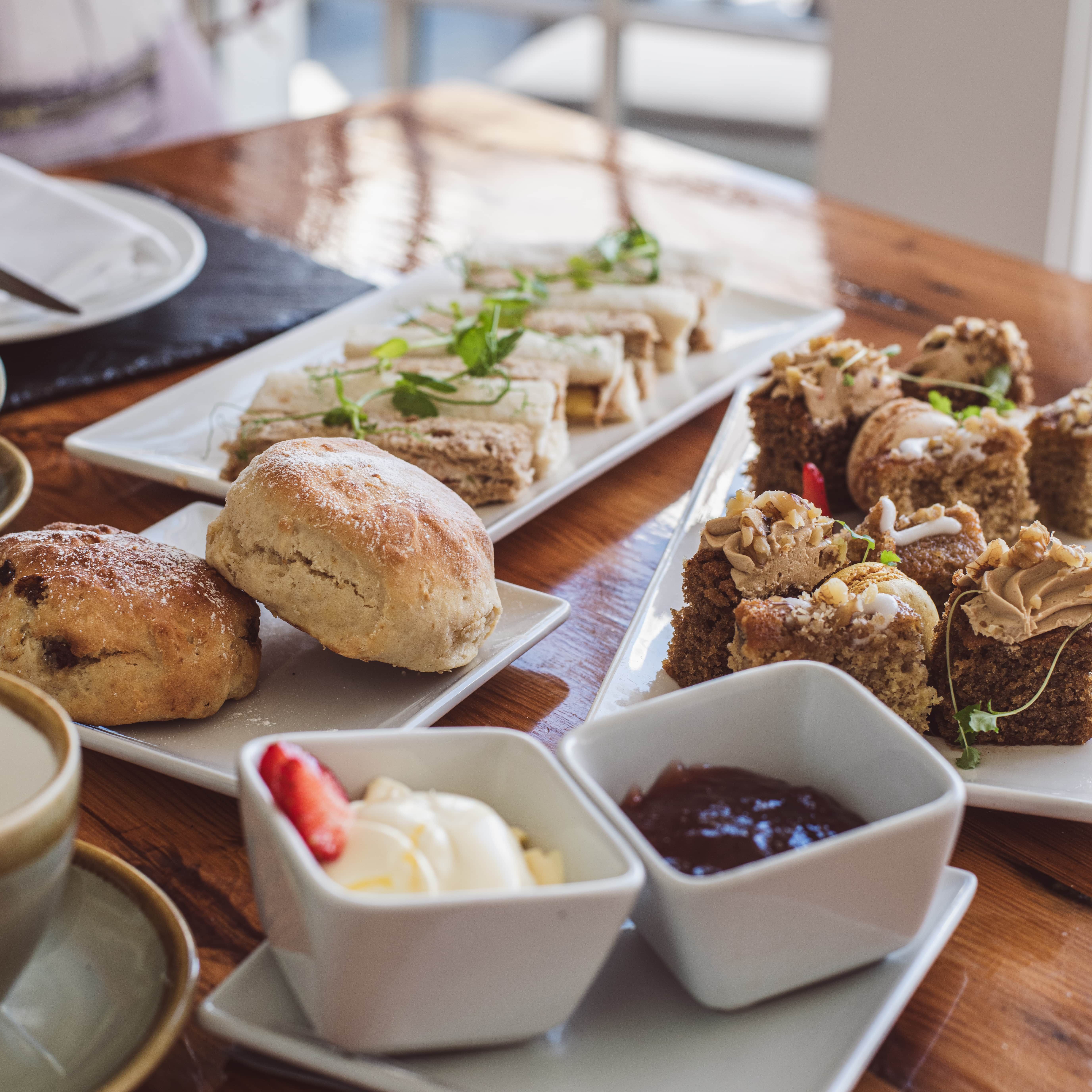 Afternoon tea with scones, finger sandwiches, cakes, clotted cream, and jam on a wooden table