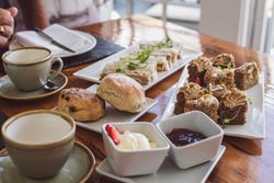 Afternoon tea with scones, finger sandwiches, cakes, clotted cream, and jam on a wooden table