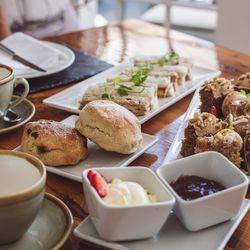 Afternoon tea with scones, finger sandwiches, cakes, clotted cream, and jam on a wooden table