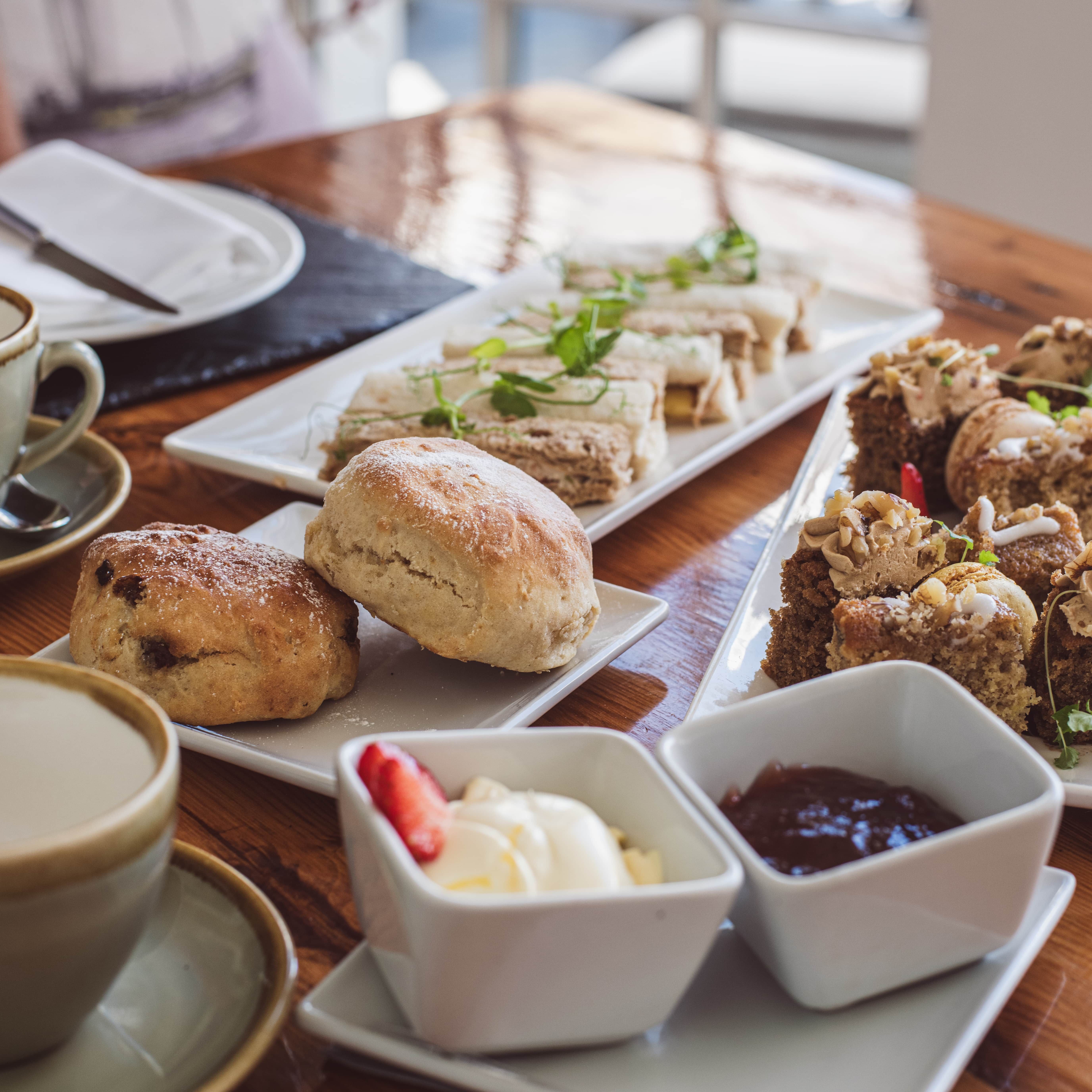 Afternoon tea with scones, finger sandwiches, cakes, clotted cream, and jam on a wooden table