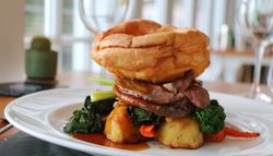 Traditional British roast dinner with Yorkshire pudding, roasted potatoes, sliced beef, broccoli, and carrots on a white plate.