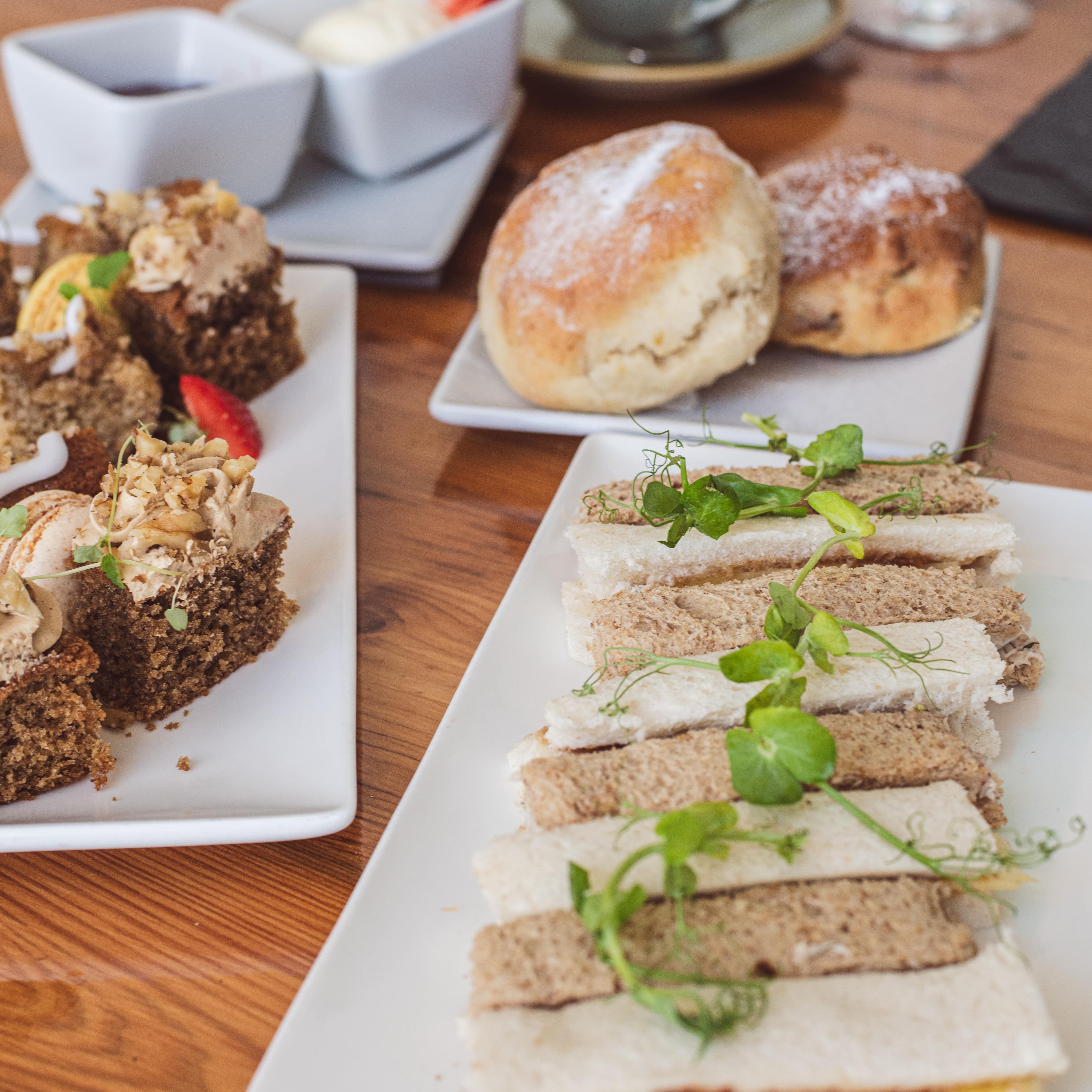 Afternoon tea with assorted finger sandwiches, scones with cream and jam, and cakes on a wooden table.
