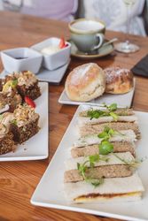 Afternoon tea with assorted finger sandwiches, scones with cream and jam, and cakes on a wooden table.