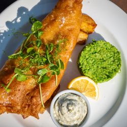 Plate of fish and chips with mushy peas, tartar sauce, and a wedge of lemon