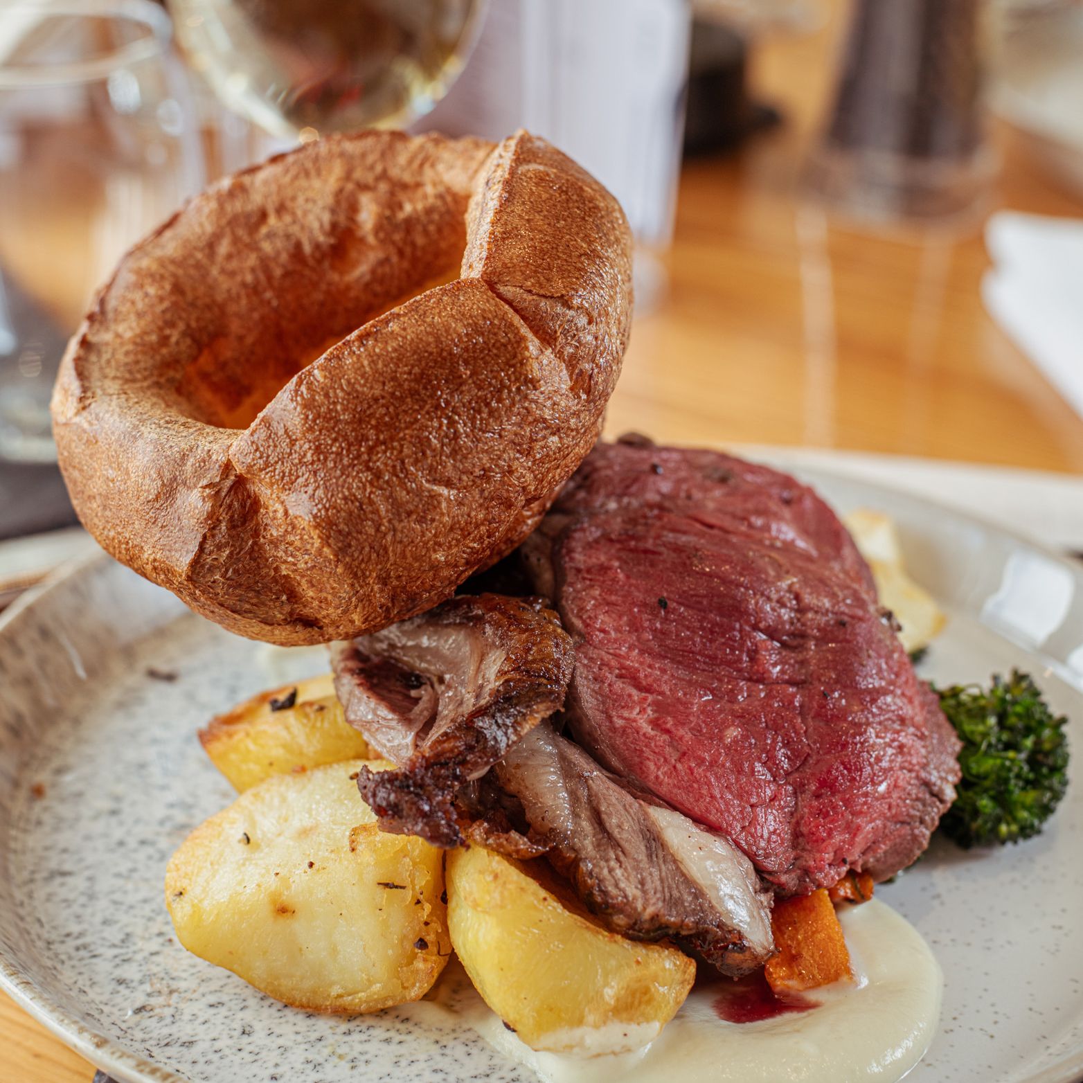 Plate of roast beef with Yorkshire pudding, roasted potatoes, vegetables, and a glass of white wine in the background.