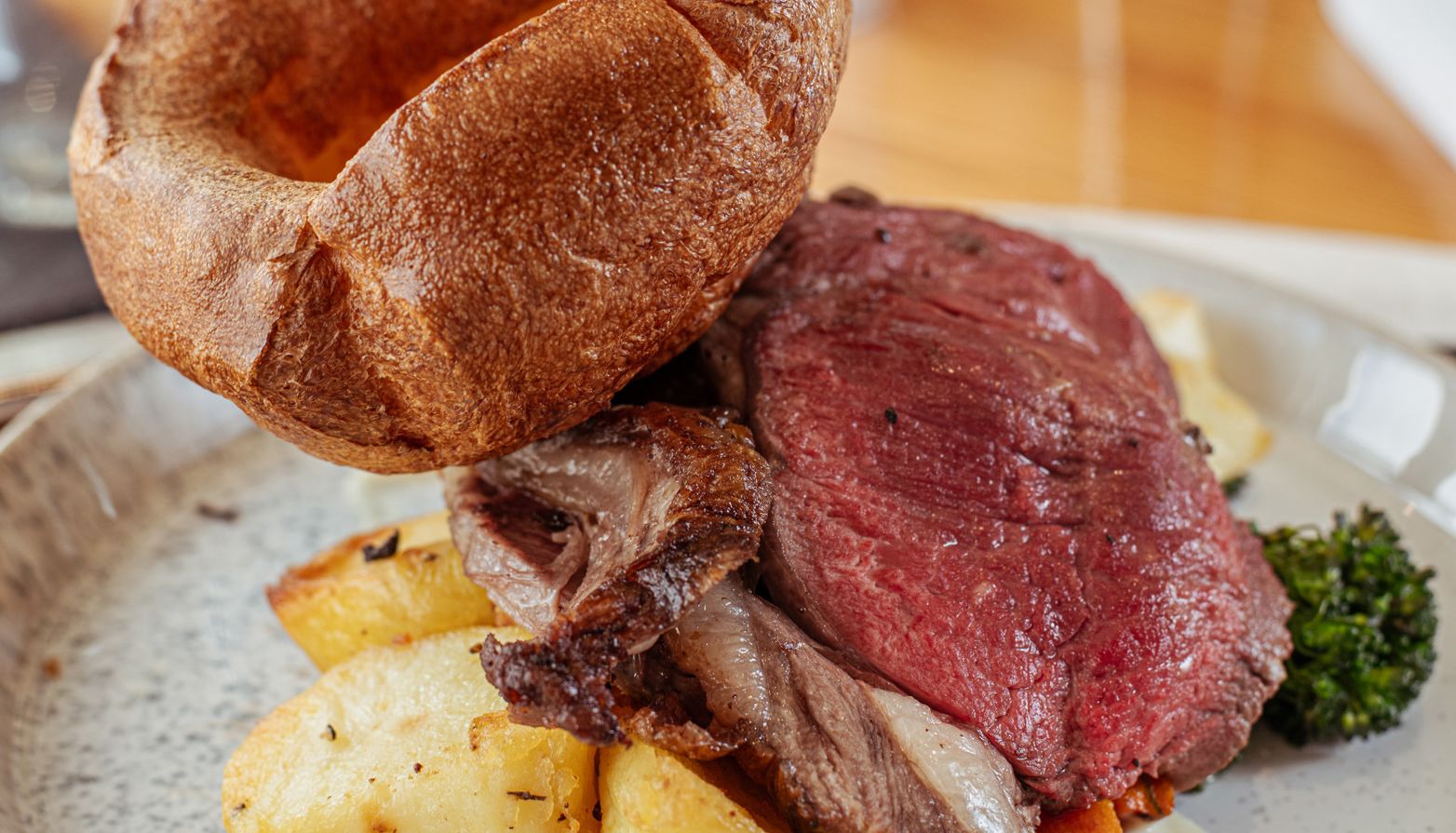 Plate of roast beef with Yorkshire pudding, roasted potatoes, vegetables, and a glass of white wine in the background.