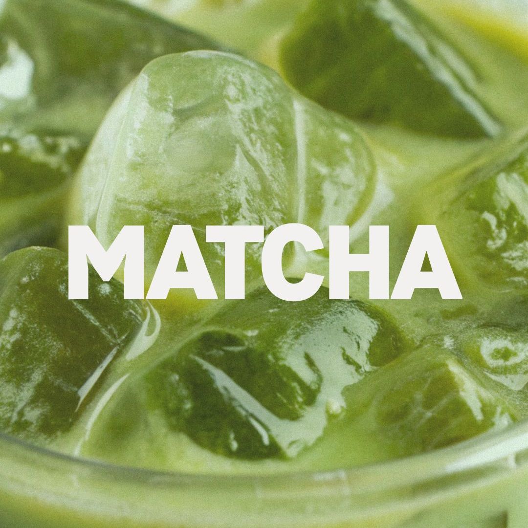 Close-up of iced matcha tea with large ice cubes in a clear glass, with the word 'MATCHA' in bold white letters.