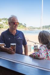 Two people enjoying drinks and conversation at an outdoor bar by the beach on a sunny day.