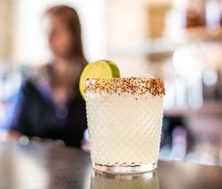 A cocktail in a textured glass with a chili salt rim and lime wedge garnish