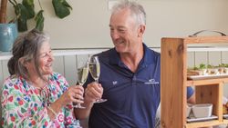 Older couple clinking champagne glasses at a table with afternoon tea