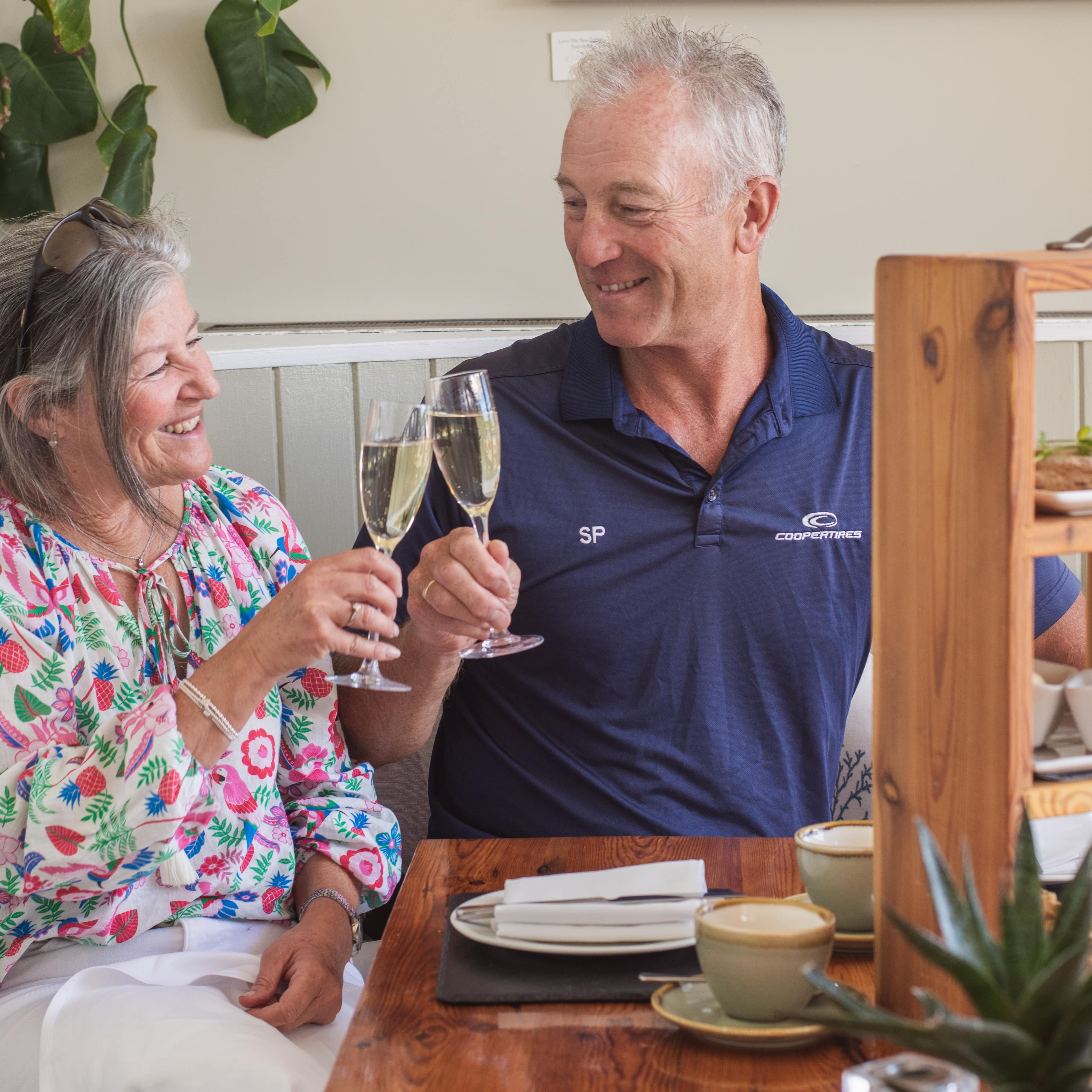 Older couple clinking champagne glasses at a table with afternoon tea