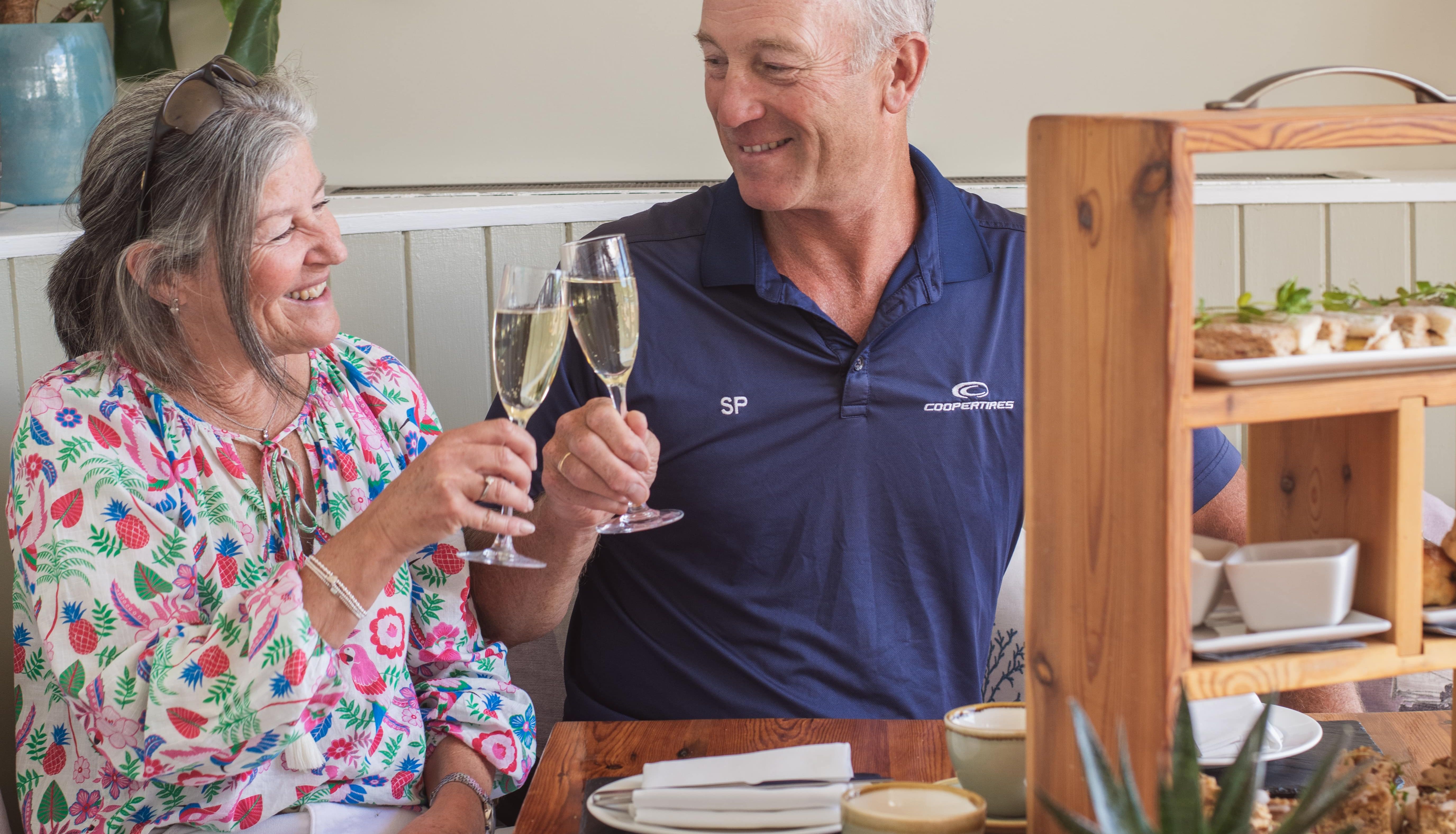 Older couple clinking champagne glasses at a table with afternoon tea