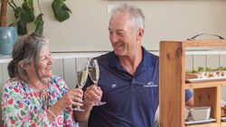 Older couple clinking champagne glasses at a table with afternoon tea
