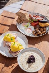 Three plates of breakfast food including eggs benedict, a traditional English breakfast, and a bowl of porridge with fruit compote.