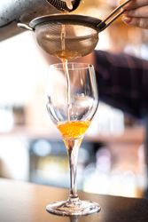 Cocktail being poured through a strainer into a wine glass
