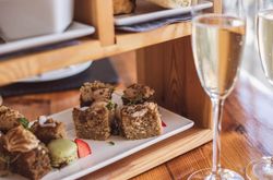 Selection of cakes and macarons on a white plate with two glasses of sparkling wine