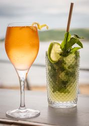 A glass of sparkling orange cocktail and a glass of mojito with lime and mint