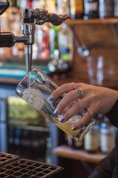 A person pouring a drink from a beer tap into a glass at a bar.