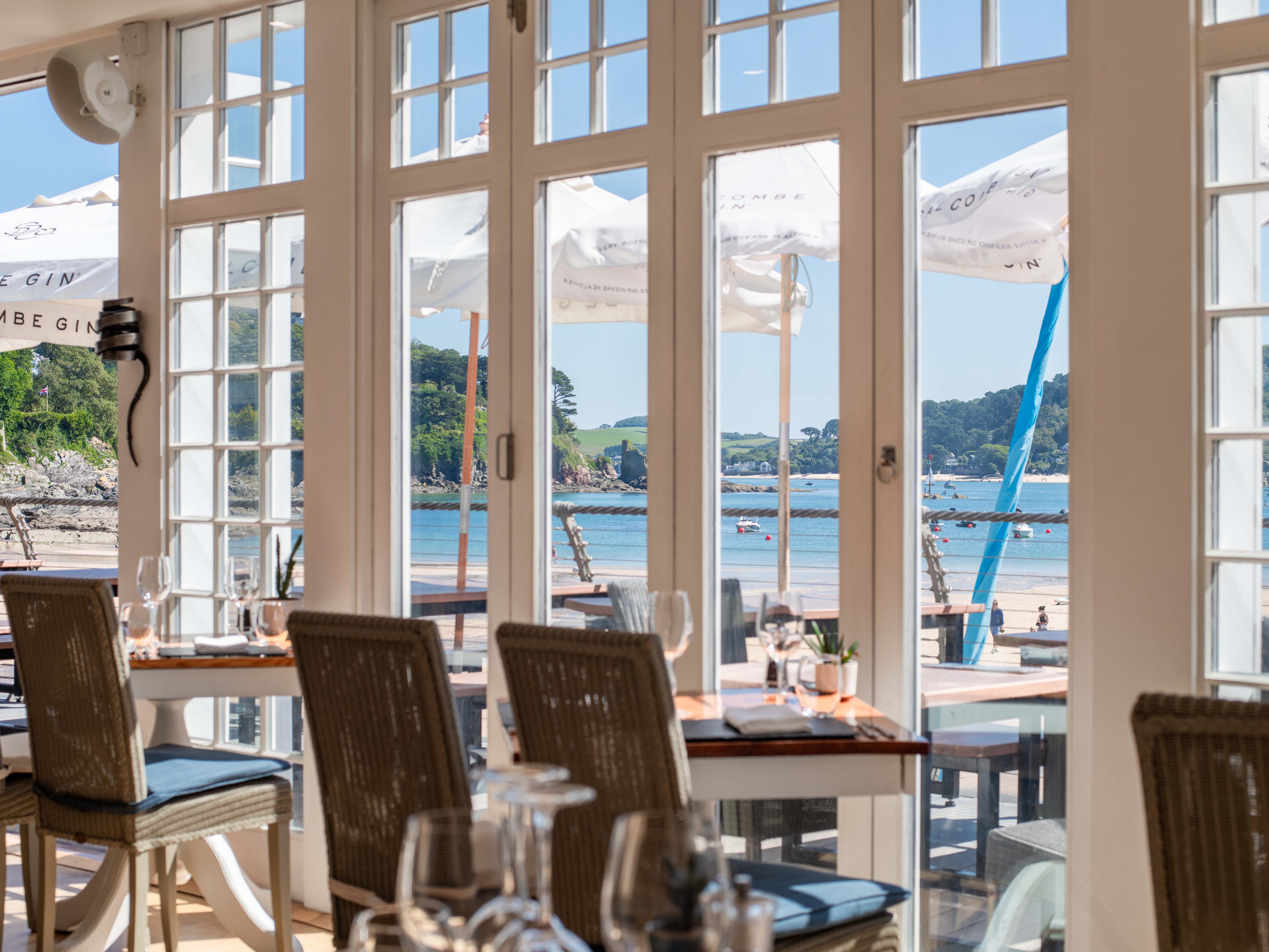 Seaside restaurant with tables near large windows overlooking a beach and ocean view