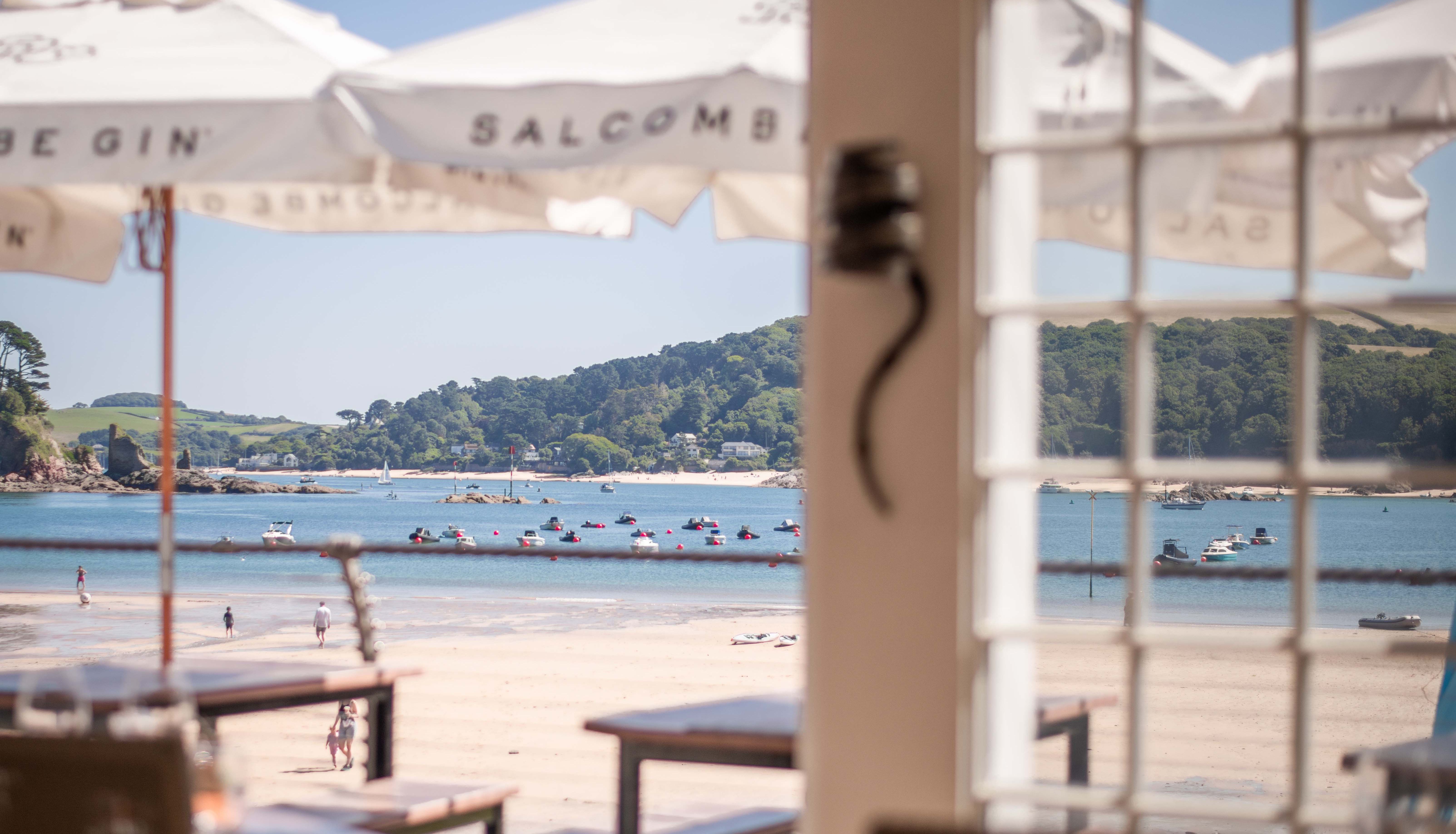 View from a seaside restaurant looking out onto a sandy beach and calm bay with boats