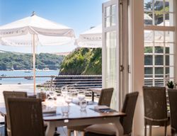 View from inside a restaurant looking out to a sunny beach and sea with outdoor umbrellas.
