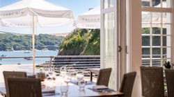 View from inside a restaurant looking out to a sunny beach and sea with outdoor umbrellas.