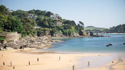 People enjoying a sunny day on a sandy beach with green cliffs and houses in the background