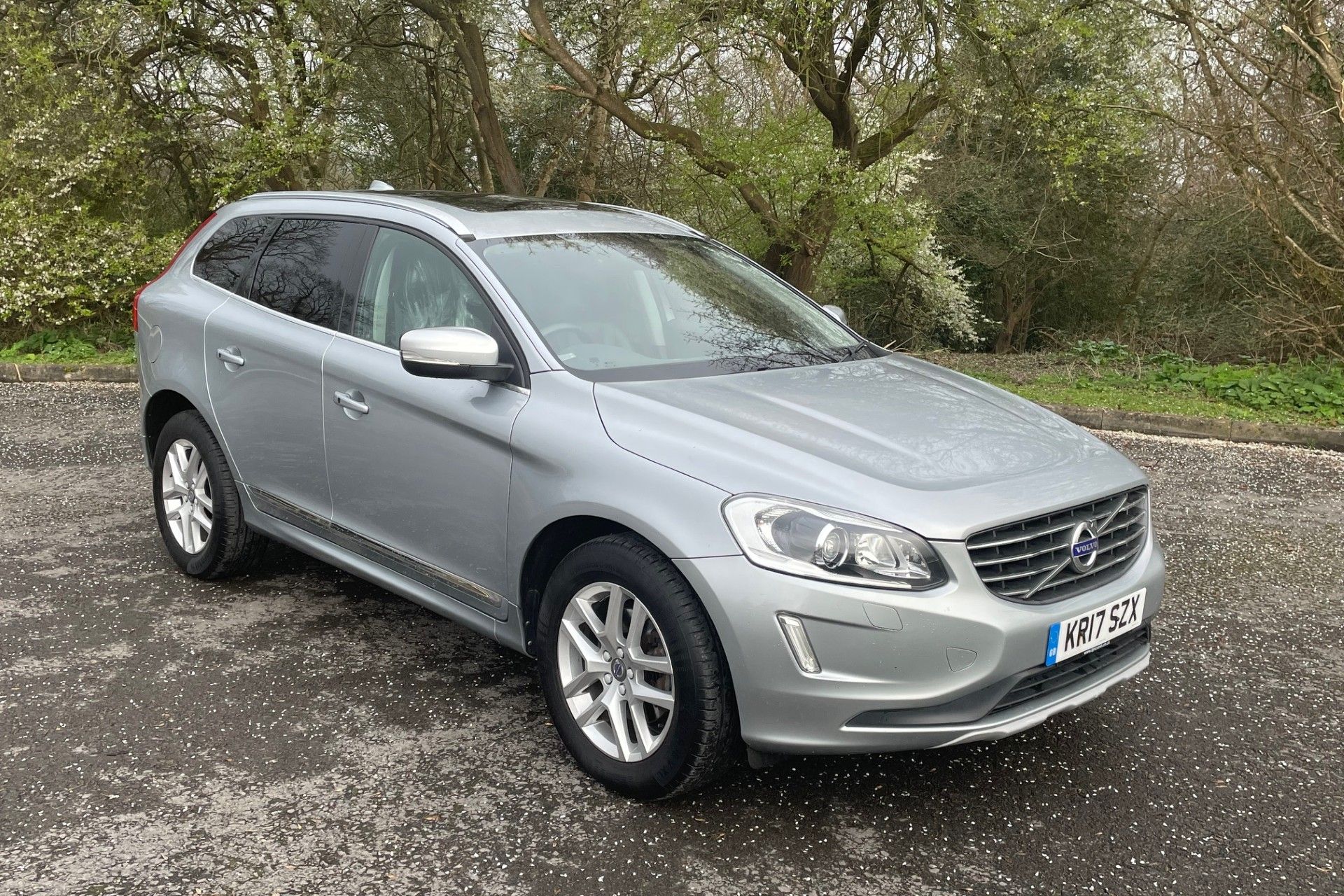 Silver Volvo XC60 SUV parked on a wet tarmac surface with trees in the background