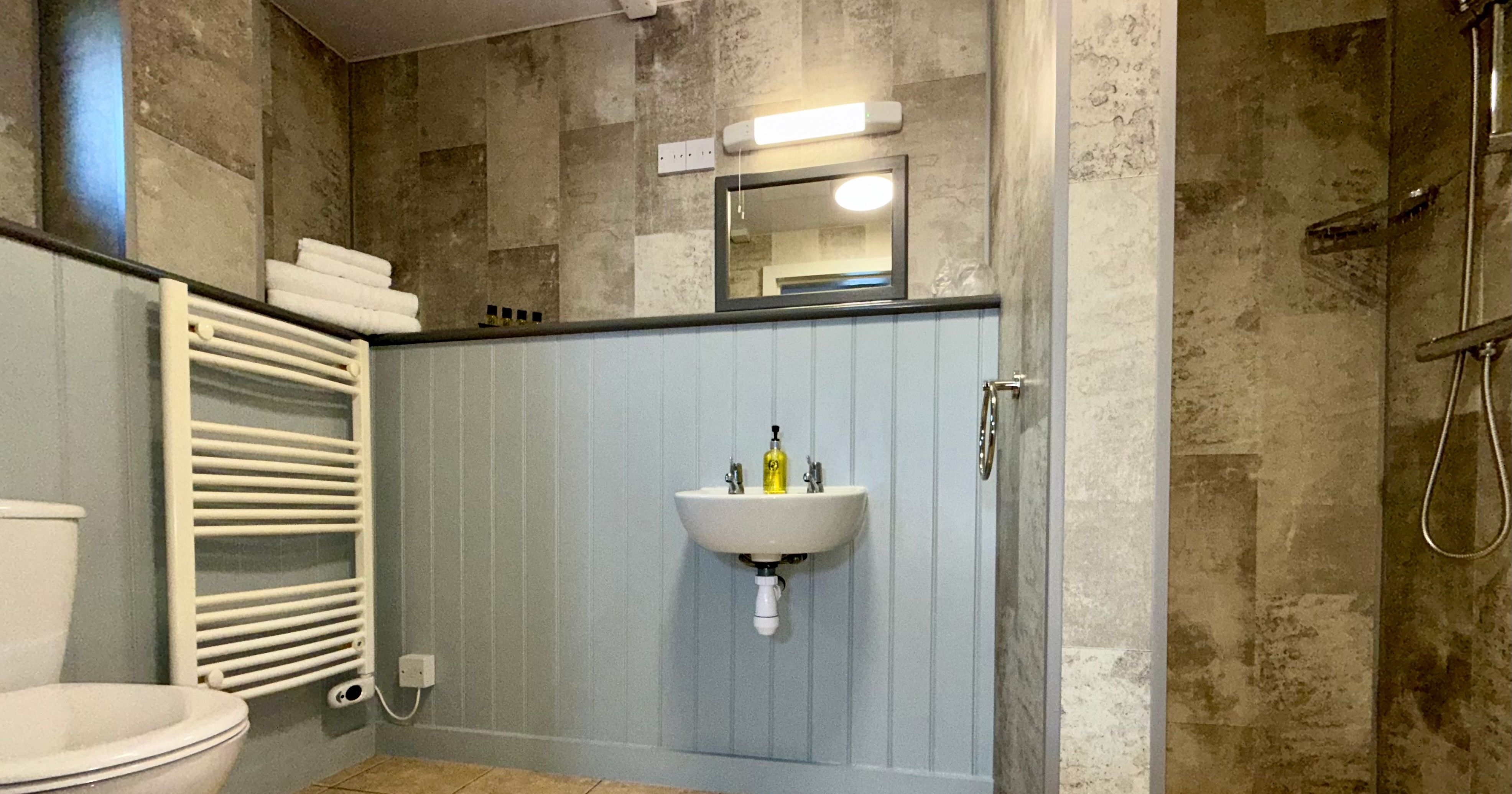Modern bathroom with tiled walls, a wall-mounted sink, walk-in shower, and a towel radiator.