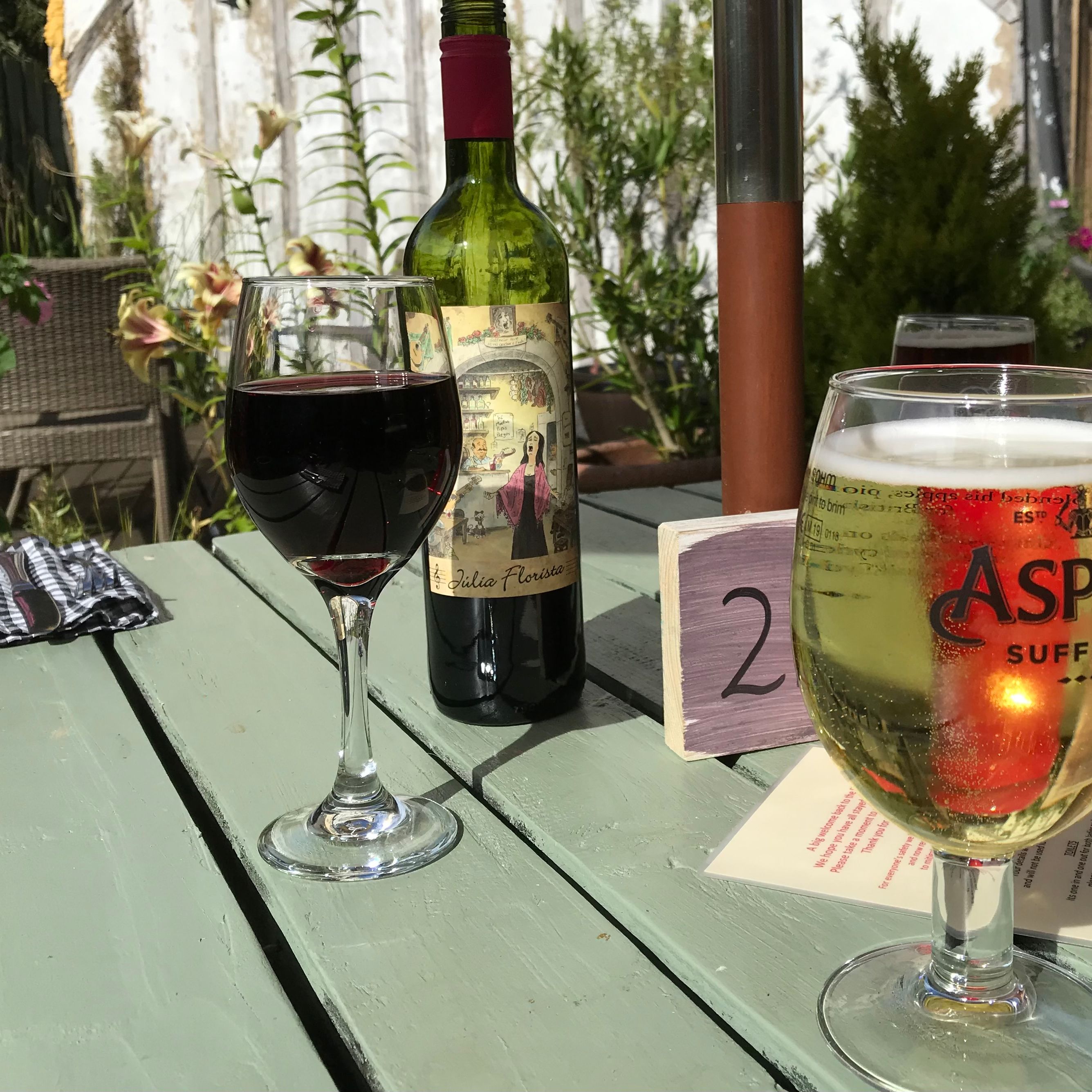 Drinks on a garden table with a glass of red wine, a glass of cider, and a wine bottle
