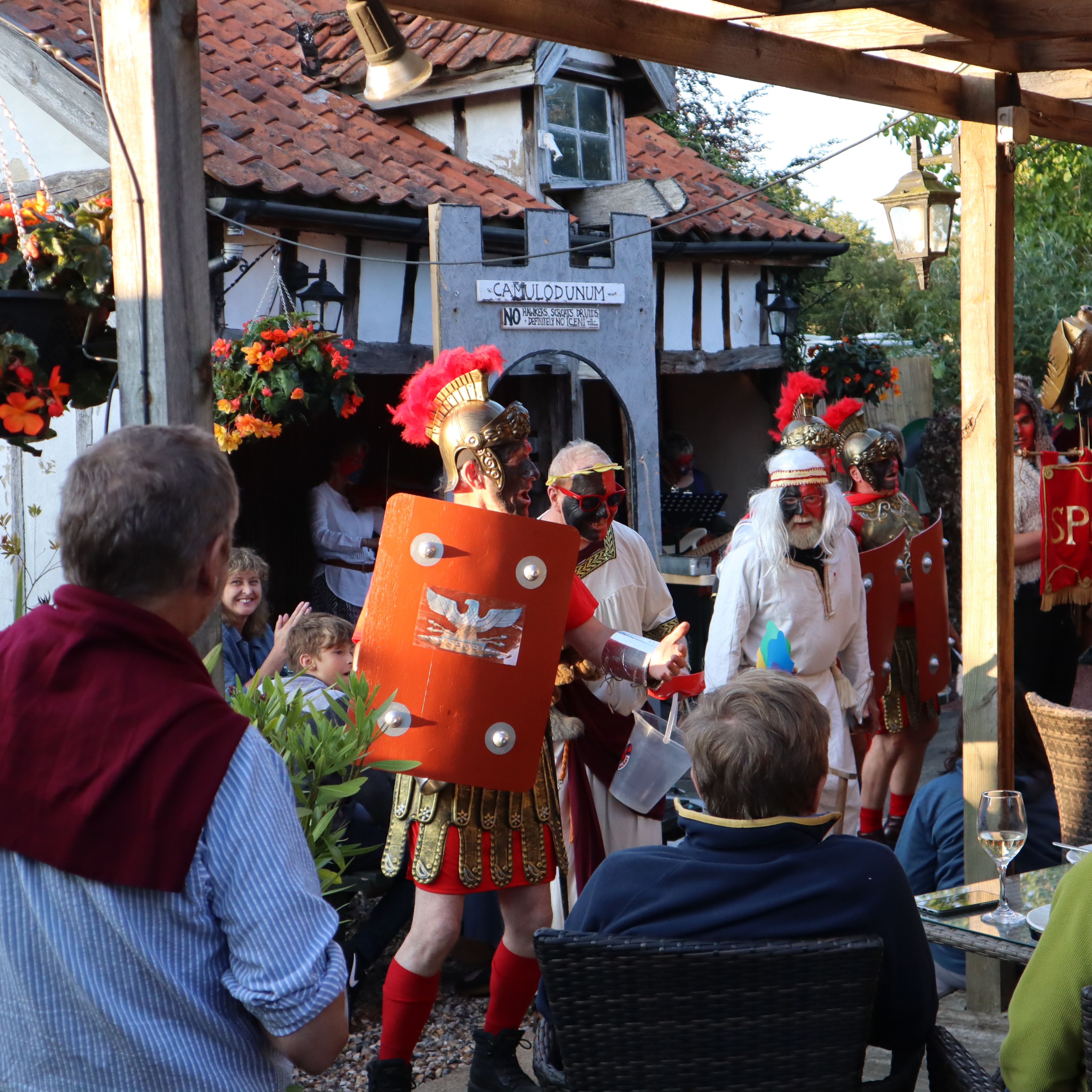 People dressed as Roman soldiers performing for an audience in an outdoor setting decorated with flowers.
