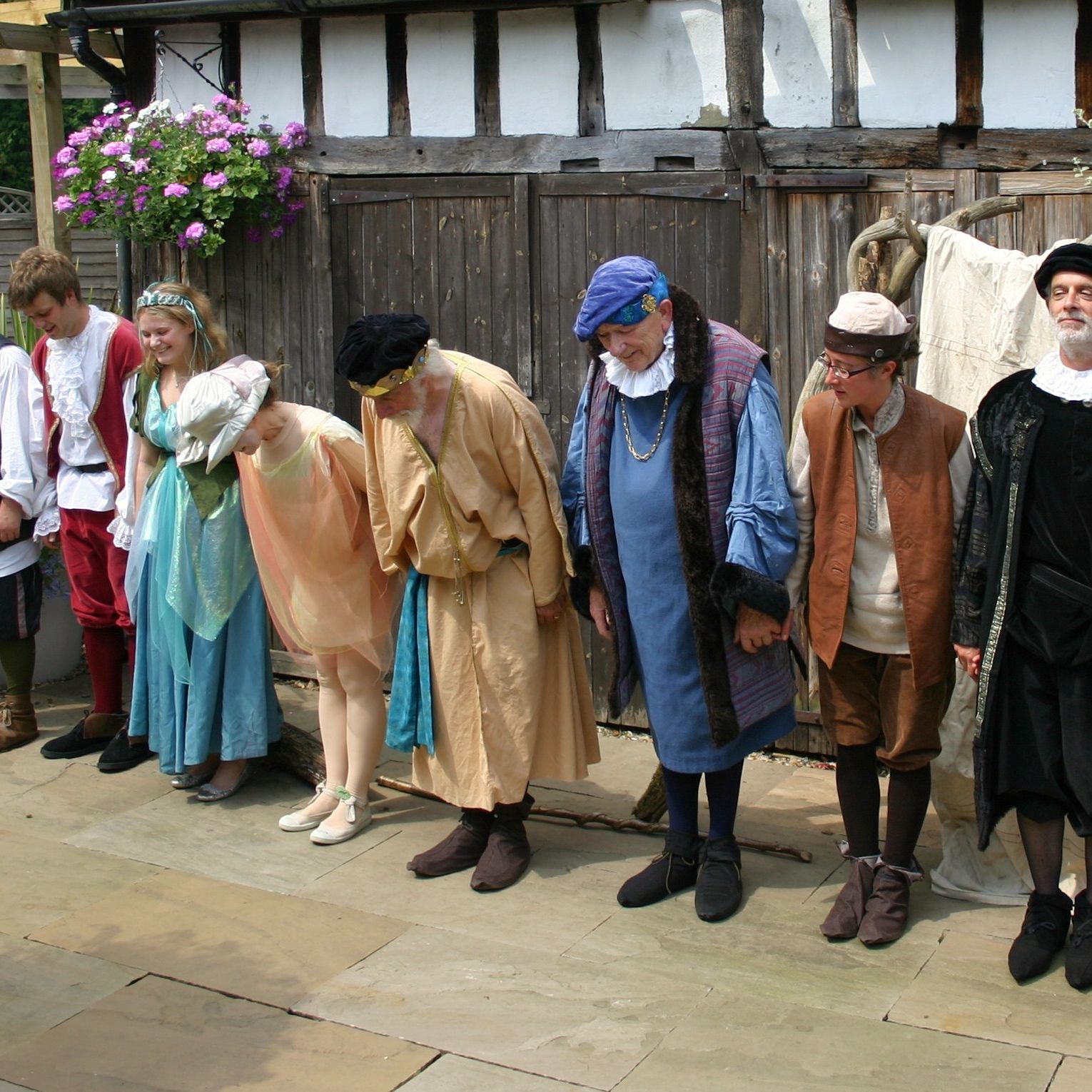 A group of people dressed in historical costumes holding hands and bowing outdoors, possibly after a stage performance.