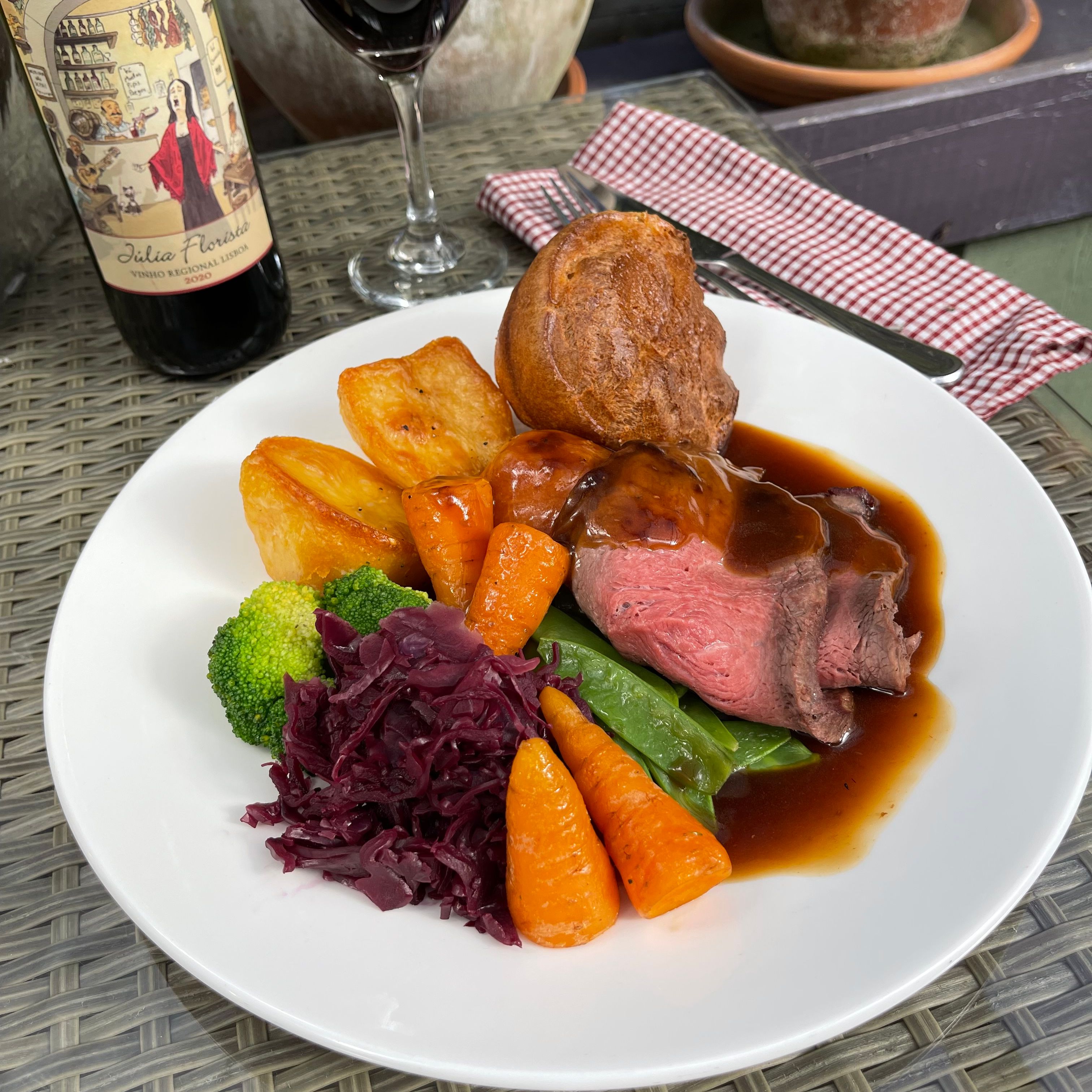 Plate of roast beef Sunday dinner with vegetables, roast potatoes, Yorkshire pudding, red wine, and bottle of wine
