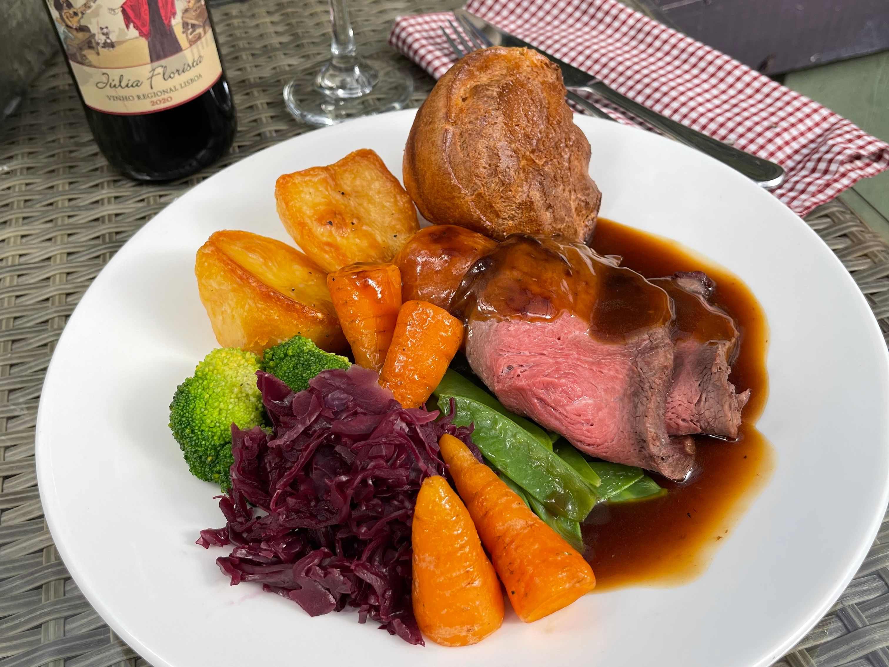 Plate of roast beef Sunday dinner with vegetables, roast potatoes, Yorkshire pudding, red wine, and bottle of wine