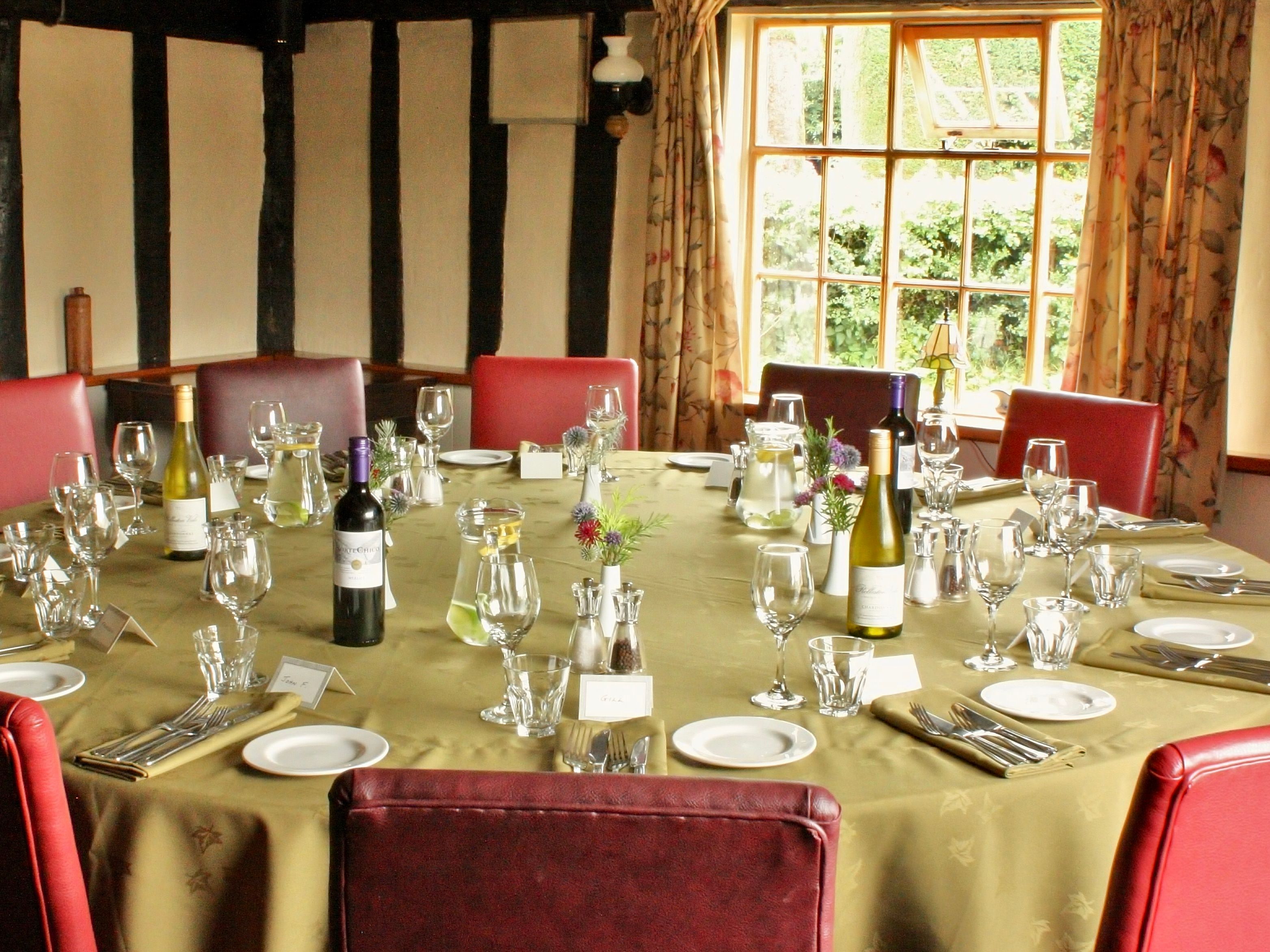 Elegant round dining table set for a meal with wine bottles, glasses, and red chairs in a sunlit room