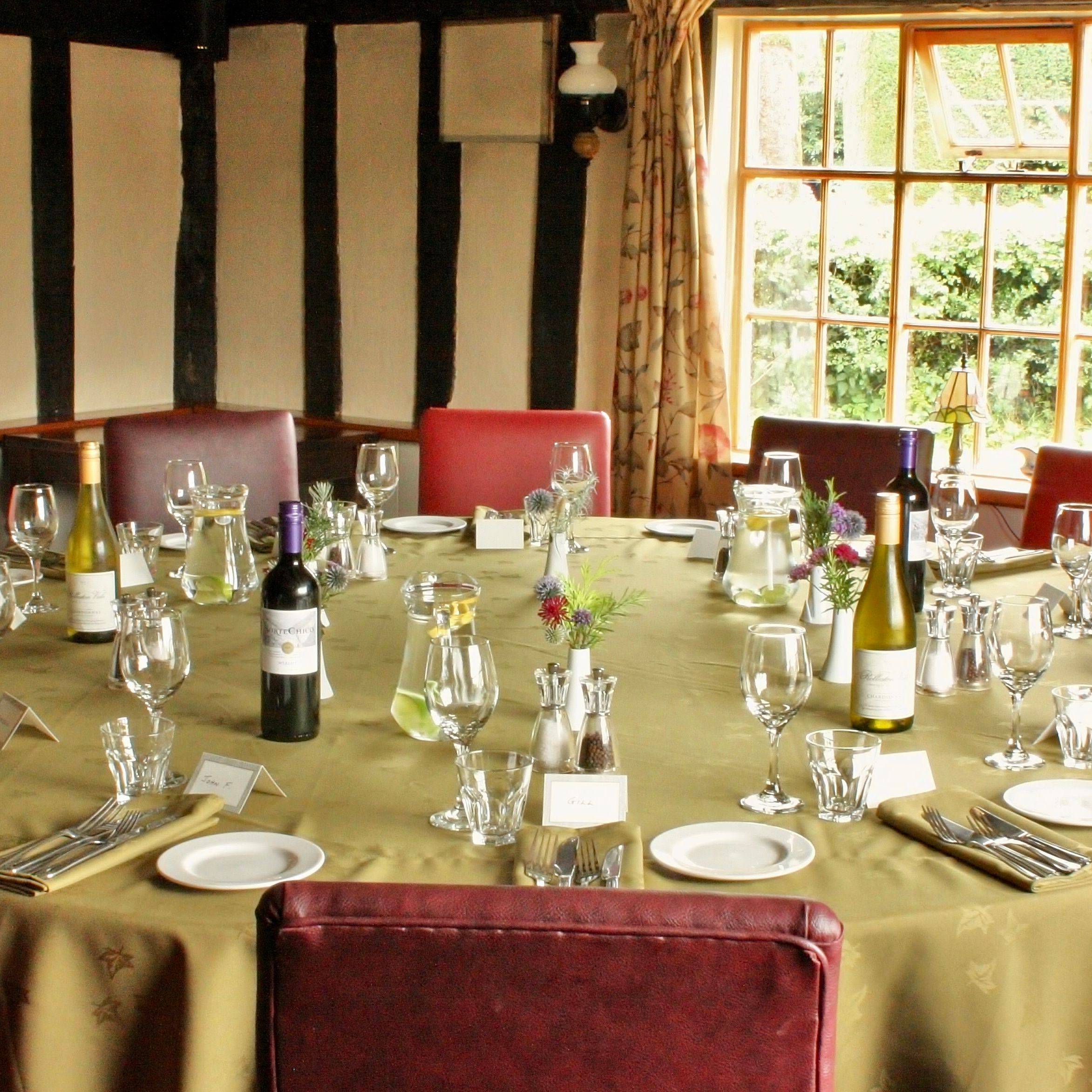 Elegant round dining table set for a meal with wine bottles, glasses, and red chairs in a sunlit room